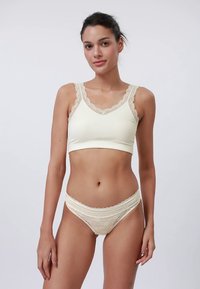 Bralet crem cu margine din dantelă pe bretele, asortat cu chiloți cu accente din dantelă. Țesătură netedă cu design ajustat.