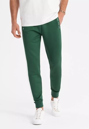 Groene sportieve joggers van gladde stof, met taps toelopende boorden en zijkanten met merkstripes. Geschoold met witte sneakers.