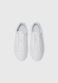 White low-top sneakers made of smooth material with round toe, laced design, and subtle branding on the tongue. Textured sole for grip.