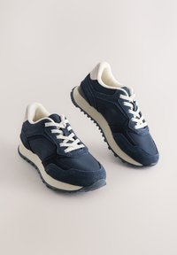 Baskets bleu marine en cuir et daim, avec des lacets blancs, un col rembourré et une semelle en caoutchouc texturée antidérapante.