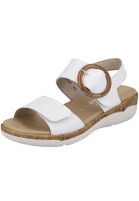 Sandal bianco con una larga fascia, chiusura in velcro regolabile e un grande elemento circolare marrone. Suola in sughero testurizzata.