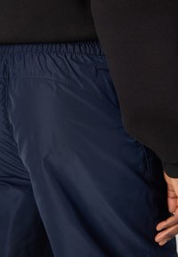 Marineblauwe, lichte, elastische taillebroek met een gladde textuur en zijzakken, gedeeltelijk weergegeven naast een zwart sweatshirt.