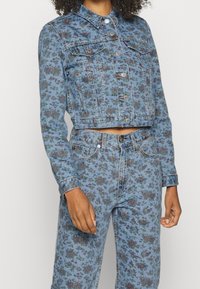 Denimjakke med blomstermønster i nuancer af blå og lilla, med en cropped design, krave og frontknaplukning.