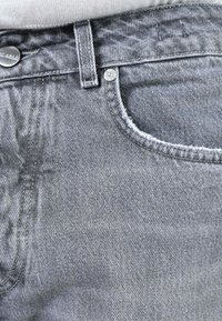Jeans in denim grigio con una texture liscia, cuciture visibili, una tasca frontale e una chiusura a bottone in vita.