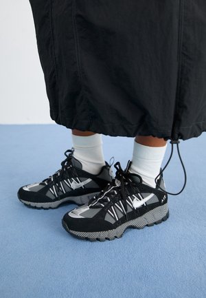 Baskets de sport noires avec des accents gris, semelle texturée et lacets blancs. Présente un motif distinctif et un logo sur le côté.