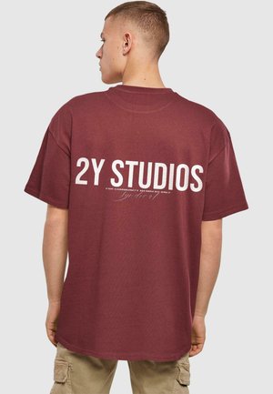 Maroon overdimensjonert t-skjorte med hvit tekst "2Y STUDIOS" på baksiden og mindre tekst under. Korte ermer og rund hals-design.