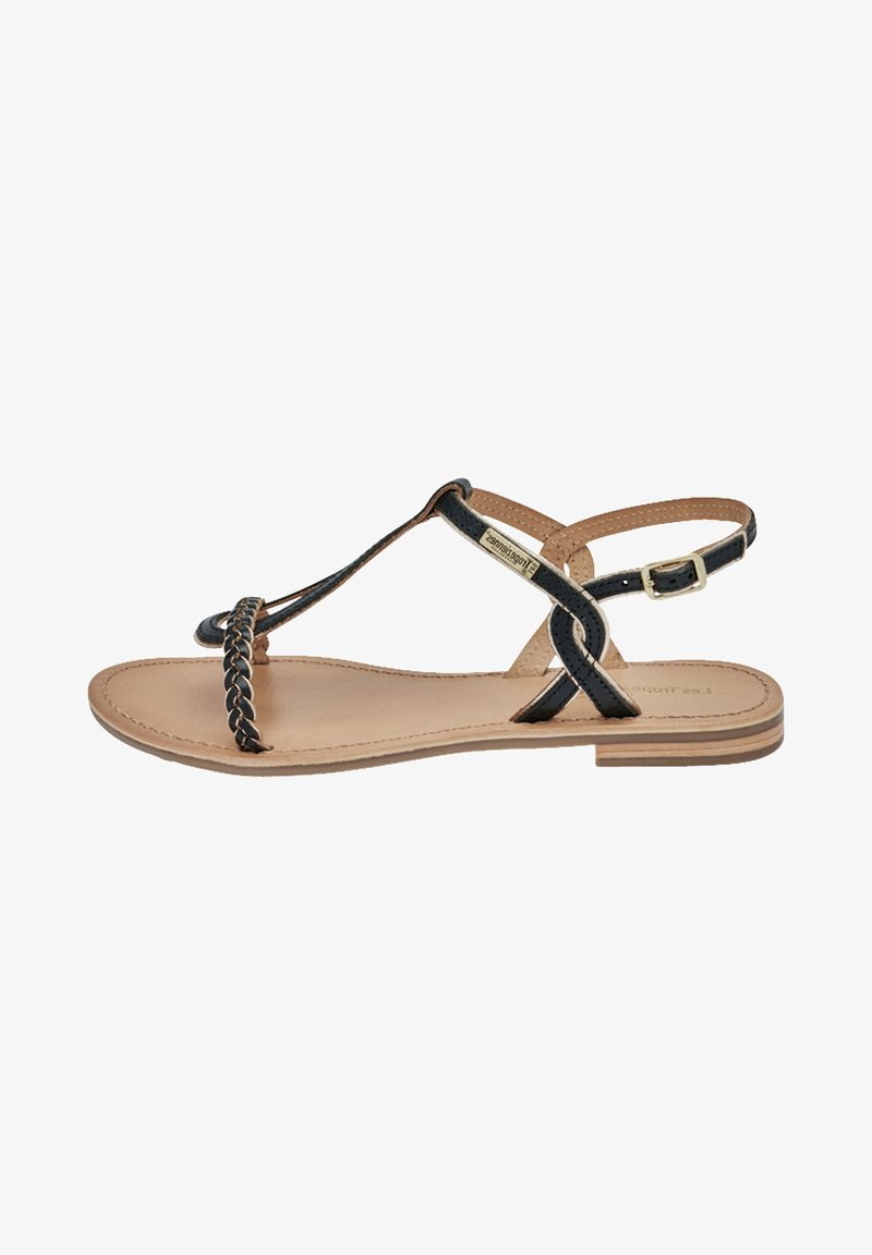 Sandal a strappo intrecciato nero con suola color cammello, caratterizzata da un design piatto, cinturino alla caviglia regolabile e dettagli minimalisti.