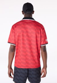 Raudonas trumpomis rankovėmis megztinis su tekstūruotu "CHICAGO" raštu, juodas apykaklė ir baltos akcentinės juostos ant rankovių. Dėvimas su tamsiais raštuotais šortais.