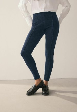 Navy blue leggings with a textured corduroy finish, featuring a high waist and a slim fit design, paired with black loafers.