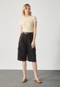 Beige short-sleeved top paired with black knee-length cargo shorts, featuring a brown belt with a round buckle and flat brown shoes.