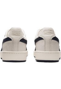 Białe skórzane sneakersy z granatowymi akcentami z tkaniny, niskoprofilowy design, okrągły czubek, gładka faktura i tonalne przeszycia na gumowej podeszwie.