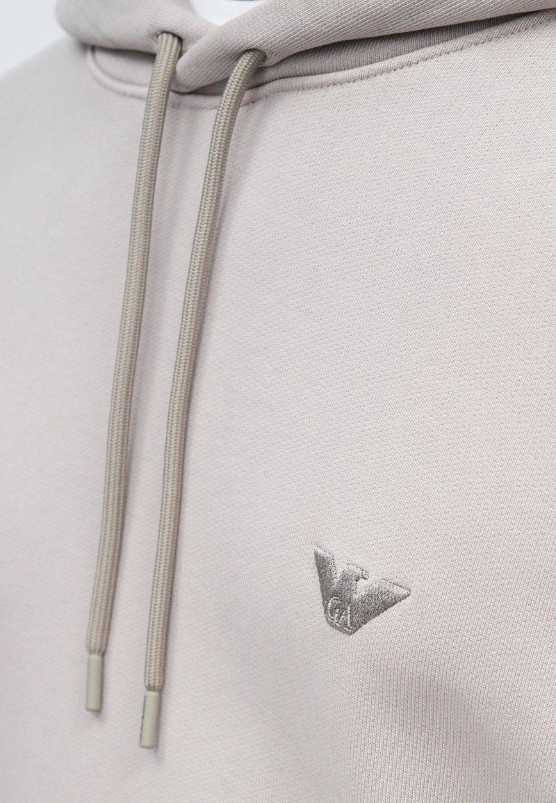 Light gray hoodie with matching drawstrings and a small embroidered logo featuring a stylized eagle and the letters "GA" on the chest.