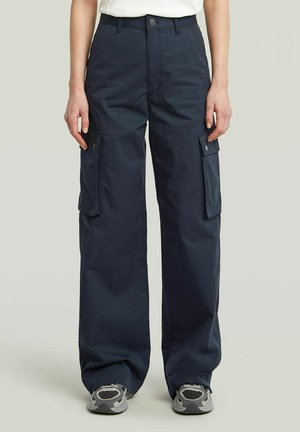 Dunkelblaue Cargo-Hosen mit weitem Bein und knöpfbaren Seitentaschen, getragen mit grauen Sneakers und einem weißen Oberteil.