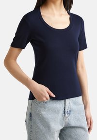 Mörkblå kortärmad t-shirt med rundad halsringning, tillverkad av mjukt material. Bärs med ljusblå jeans med dekorationer.