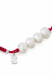 Pulsera de perlas con cuatro grandes perlas blancas sobre un cordón trenzado rojo, que presenta un pequeño charm de oso de plata como acento decorativo.