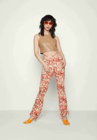 Top cropped de couro castanho, calças com padrão ondulado multicolorido, sandálias de salto alto laranja e óculos de sol laranja. Textura suave e design ajustado.
