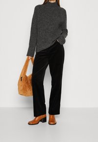 Pull en maille gris, pantalon en velours côtelé noir, bottes à talons brunes et sac à main orange duveteux. Mettez l'accent sur la texture et le contraste des couleurs.