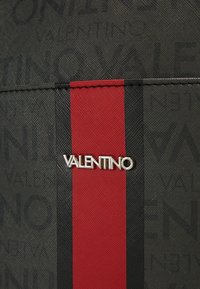 Black textured fabric with repeating "Valentino" pattern, featuring a central red stripe and silver "Valentino" logo accent.