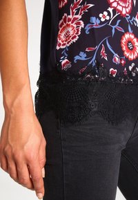 Černá květinová halenka s vzorovanou tkaninou v odstínech červené a modré, s krajkovou lemovkou na spodním okraji a přiléhavým střihem.