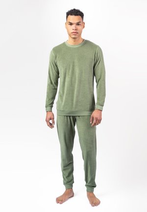 Man standing barefoot wearing matching green long-sleeve top and pants against a plain white background.