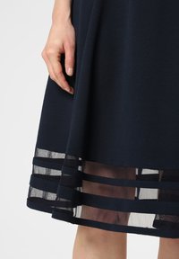 Marineblaues Kleid aus strukturiertem Stoff, mit einem transparenten Saum und horizontalen Streifen. Der Rock weitete sich sanft von der Taille.