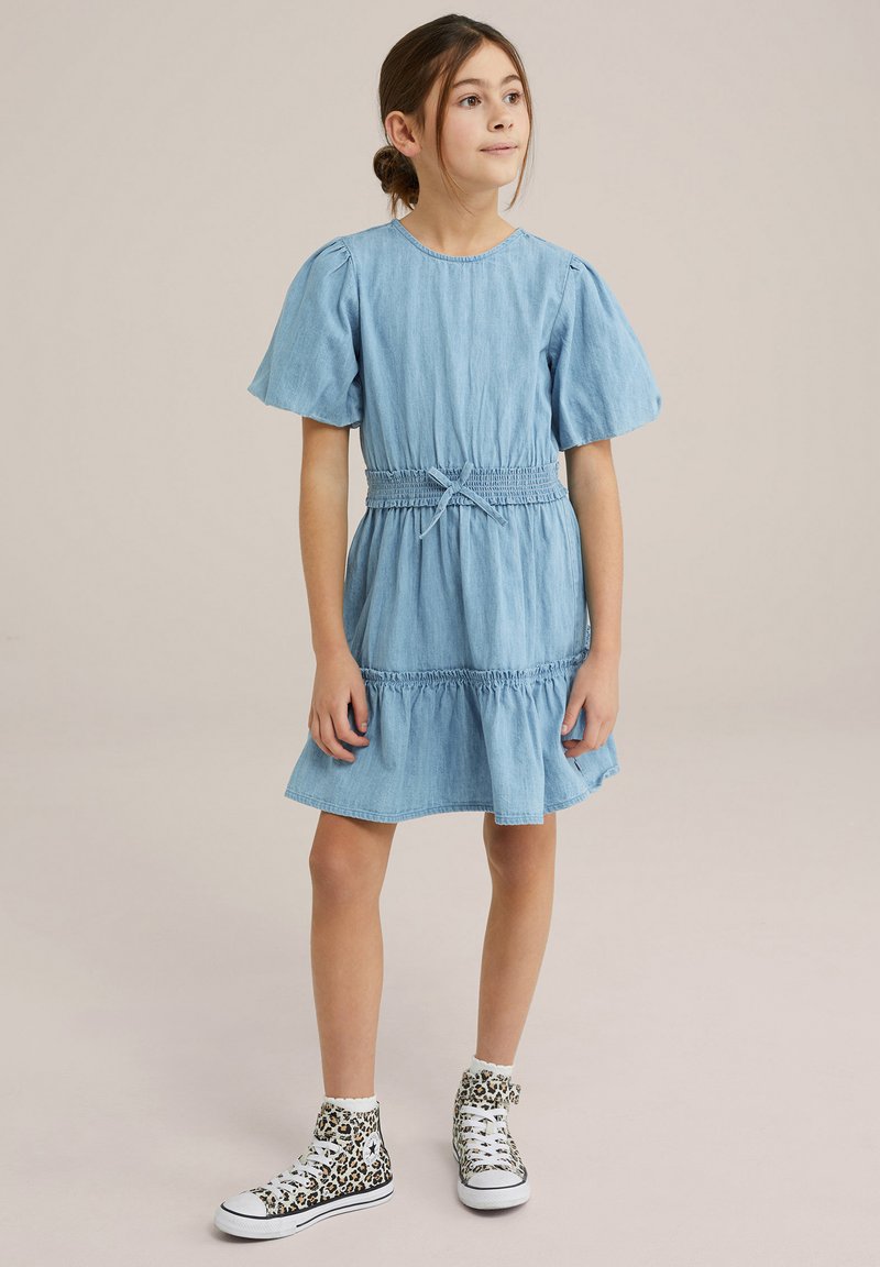 Svetlo modra jeans obleka s kratkimi napihnjenimi rokavi in cinčanim pasom, ki vključuje zbrano krilo. V kombinaciji z visokimi superge v leopardjem vzorcu.