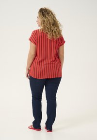 Top de manga corta a rayas rojas con un corte holgado, combinado con jeans ajustados azul oscuro y chanclas rojas. Tejido ligero y texturizado.
