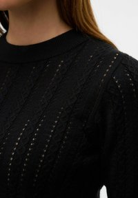 Černý pletený svetr se vzorovaným výstřihem a texturovaným designem s otevřenými kabelovými vzory, který zdůrazňuje vertikální linie a poskytuje prodyšný pocit.