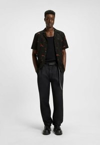Korte mouwen zwarte shirt met rode bloemenpatronen, gedragen over een zwarte tanktop, gecombineerd met losse zwarte broeken en zwarte schoenen.