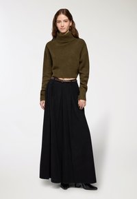Maglione a collo alto verde oliva cropped abbinato a una gonna lunga plissettata nera e una cintura marrone, caratterizzato da una texture liscia e una silhouette aderente.