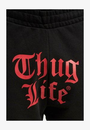 Fekete melegítőnadrág, hátulján nagy piros felirattal, amely „Thug Life” felirattal büszkélkedik, vastag, stílusos betűtípussal. Puha anyag, rugalmas derékrésszel.