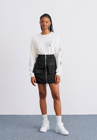 Long-sleeve white shirt with printed designs and a black zip-up skirt featuring pockets, paired with white sneakers and crew-length socks.