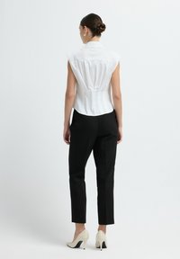 Witte mouwloze blouse met een hoge kraag, met achterplooien, gecombineerd met zwarte op maat gemaakte broeken en crèmekleurige hakken.