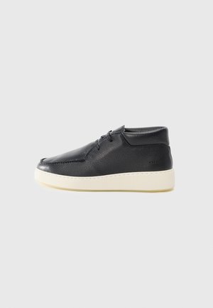 Black leather high-top shoe with textured surface, rounded toe, and white rubber sole. Features laces on the front and subtle stitching accents.