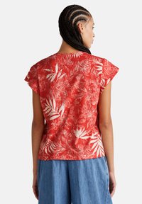Top de estampado floral rojo con mangas cortas, que presenta un corte holgado y una tela texturizada. La vista trasera muestra un dobladillo curvado.