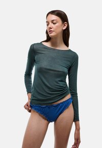 Haut à manches longues vert foncé avec encolure dégagée et détail froncé, associé à une culotte bleue à volants, présenté sur fond blanc.