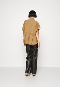 Top peplum marrone con colletto alto e maniche corte, abbinato a pantaloni in pelle neri a gamba larga e scarpe taupe a punta.
