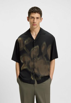 Short-sleeve black button-up shirt with a blurred floral print in beige. Smooth fabric, relaxed fit, with a conventional collar and front pockets.