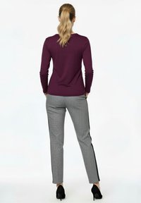 Lila Langarmshirt kombiniert mit gemusterten grauen Hosen mit schwarzen Seitenstreifen, dazu schwarze High Heels. Von hinten gestylt.