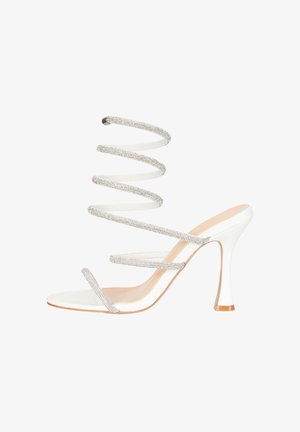 Weiße Sandalette mit hohem Absatz und mehreren dünnen, funkelnden Riemchen, inklusive einem spiralförmigen Knöchelriemen, und einer beigen Sohle mit spitzer Absatzspitze.