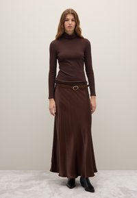 Brown ribbed turtleneck top paired with a flowing brown maxi skirt, cinched at the waist with a suede belt featuring a circular buckle. Black ankle boots.