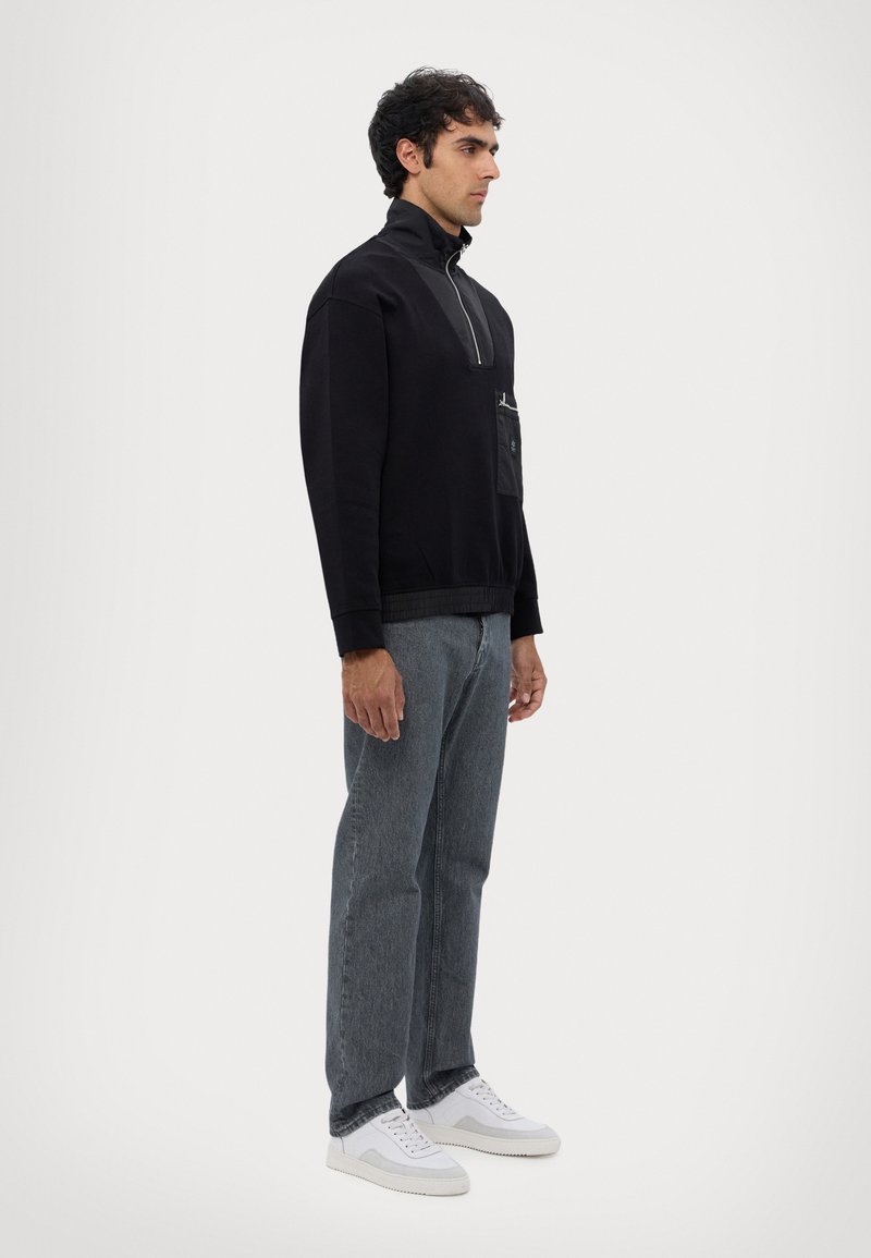 Felpa nera con zip e tasca frontale, abbinata a jeans in denim grigi e sneakers bianche. Texture liscia, vestibilità comoda.