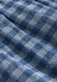 Tissu à carreaux vichy bleu et blanc avec un tissage texturé, présentant des carreaux alternés dans différentes nuances de bleu, créant un effet de superposition.