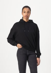 Zwarte hoodie van een katoenmix met trekkoord, geborduurd logo op de voorkant, relaxte pasvorm, geribde manchetten en zoom. Draagt het met donkere jeans.