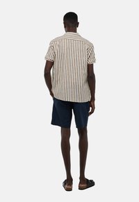 Chemise à col à manches courtes avec des rayures verticales blanches et brunes, associée à un short bleu marine. Le matériau semble léger et texturé.