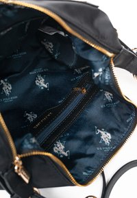 Sort håndtaske indvendigt med blå stofforing med hvide U.S. Polo Assn. logoer, en lynlåslomme og guld lynlåse.