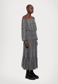 Šedé off-shoulder šaty s dlouhým rukávem a vzorem hadí kůže. Mají smyčkový pas a splývavý střih, doplněné o masivní černé boty.