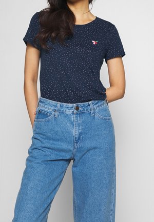 Mørkeblå t-shirt med korte ærmer med små flerfarvede prikker og en rød, grøn og pink broderet detalje, kombineret med lyseblå, høj-taljede jeans.