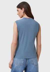 Top senza maniche in cotone blu con scollatura rotonda e texture liscia. Presenta un orlo dritto ed è abbinato a jeans in denim chiaro.