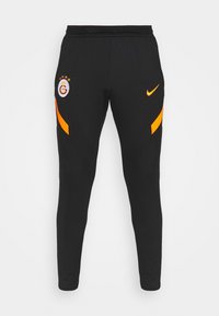 Czarne spodnie sportowe z pomarańczowymi paskami, logo Nike na prawej uda oraz herb klubu piłkarskiego Galatasaray na lewej udzie.